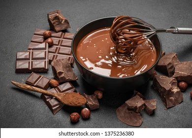 Melted chocolate being whisked in a ceramic bowl with chocolate around the bowl